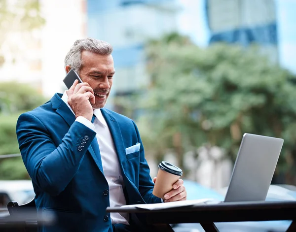 Puo 'lavorare ovunque, e' il capo. Girato di un bell'uomo d'affari maturo in abbigliamento aziendale su una chiamata e utilizzando un computer portatile fuori durante il giorno. — Foto Stock