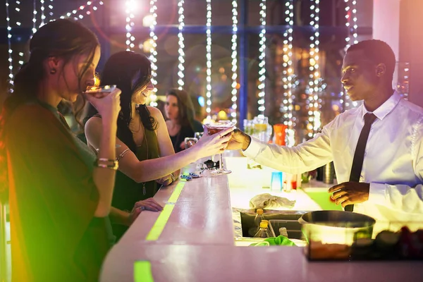 Deze is van het huis. Schot van een barman die een drankje overhandigt aan een jonge vrouw over de bar. — Stockfoto