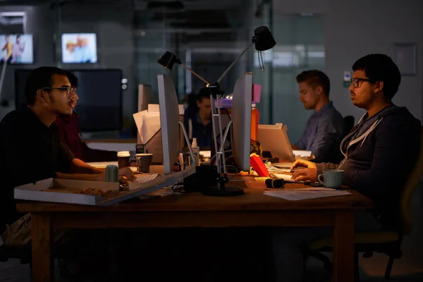 Portare a termine il lavoro. Foto ritagliata di un gruppo di giovani colleghi che lavorano in un ufficio scarsamente illuminato. — Foto Stock