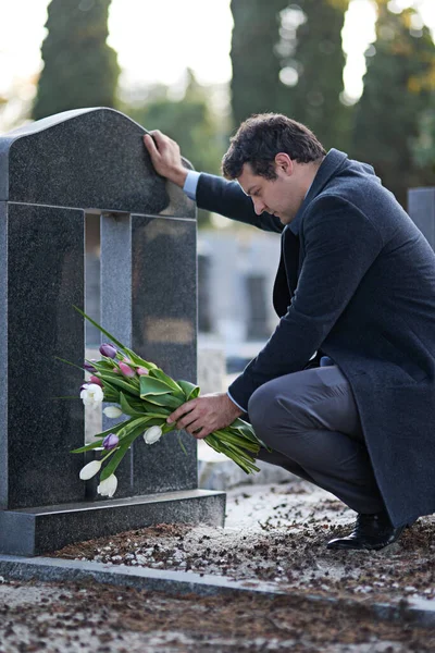Это были её любимые цветы. Фотография молодого человека, посещающего могилу с букетиком цветов. — стоковое фото