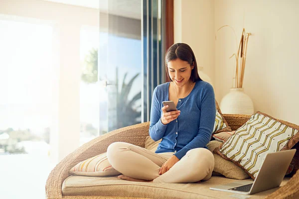 Die Welt vom bequemen Sofa aus sehen. Aufnahme einer glücklichen jungen Frau, die ihr Smartphone benutzt, während sie sich in ihrer Lounge zu Hause entspannt. — Stockfoto