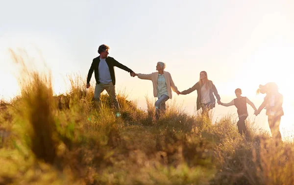 Nagyapa vezet. Egy többgenerációs családról, akik kéz a kézben sétálnak a mezőn naplementekor.. — Stock Fotó