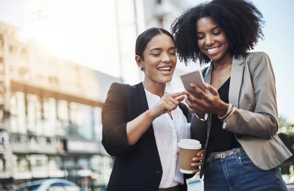 Raggiungere nuove reti. Due donne d'affari che guardano qualcosa su un cellulare in citta '.. — Foto Stock