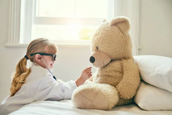 Das ist ein gutes Herz, das du da hast, Teddy. Aufnahme eines entzückenden kleinen Mädchens, das sich als Arzt verkleidet und einen Teddybär mit einem Stethoskop untersucht. — Stockfoto