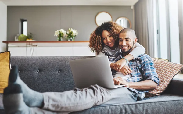 Ihre Verbindung lässt sich nicht leugnen. Aufnahme einer jungen Frau, die ihren Mann umarmt, während er zu Hause auf dem Sofa einen Laptop benutzt. — Stockfoto