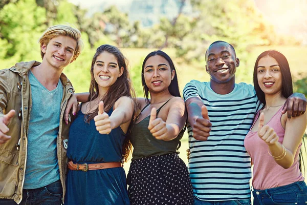 Pulgares a amistades duraderas. Retrato de un grupo de jóvenes amigos mostrando los pulgares hacia arriba mientras pasan el rato juntos en el parque. — Foto de Stock