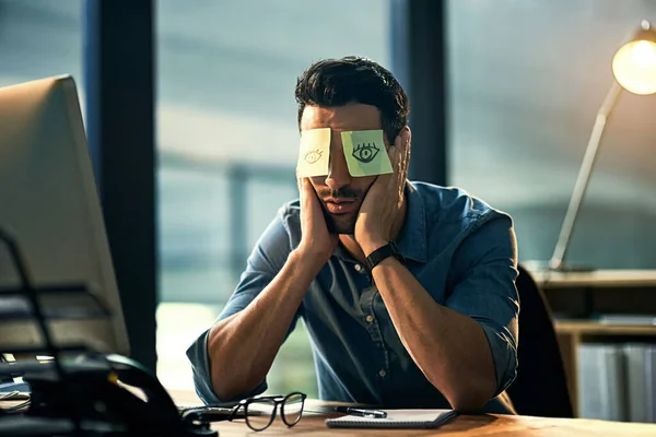 Pas le temps de dormir. Prise de vue d'un jeune homme d'affaires fatigué travaillant tard dans un bureau avec des notes adhésives couvrant ses yeux. — Photo