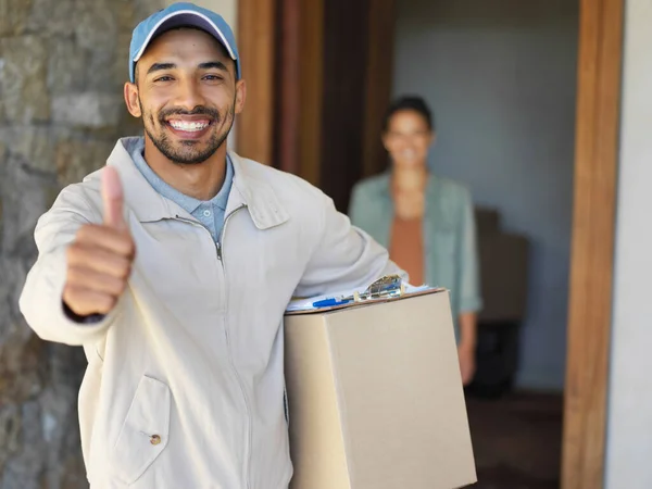 You can count on us to get your packages delivered. Portrait of a smiling young courier giving a thumbs up and carrying a package with a customer standing at her front door in the background.