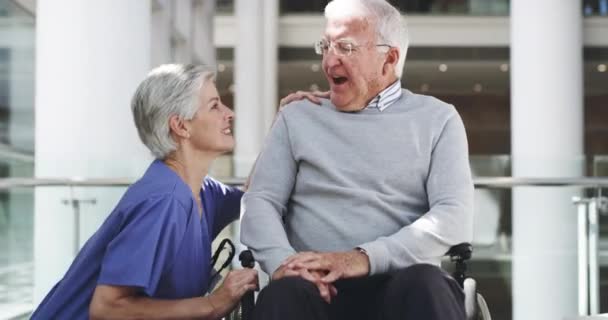¿Cómo te va? Imágenes de video de 4k de una enfermera madura hablando con un paciente varón mayor en silla de ruedas. — Vídeos de Stock