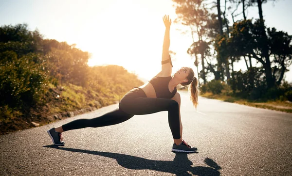 A pôr a mente e os músculos na zona de treino. Tiro de uma jovem mulher apta que se estende antes de uma corrida ao ar livre. — Fotografia de Stock