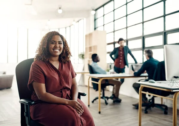 A siker kulcsa a pozitivitás. Egy fiatal üzletasszony portréja, aki egy modern irodában ül a kollégáival a háttérben.. — Stock Fotó