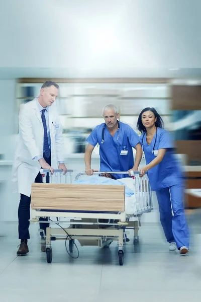 Naar de operatiekamer. Een foto van een groep medische professionals die een patiënt op een brancard door een ziekenhuisgang joegen.. — Stockfoto