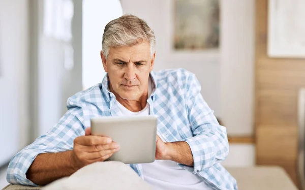 Desplazamiento a través de sitios web. Tiro de un hombre maduro usando su tableta digital mientras se relaja en su sofá en casa. —  Fotos de Stock