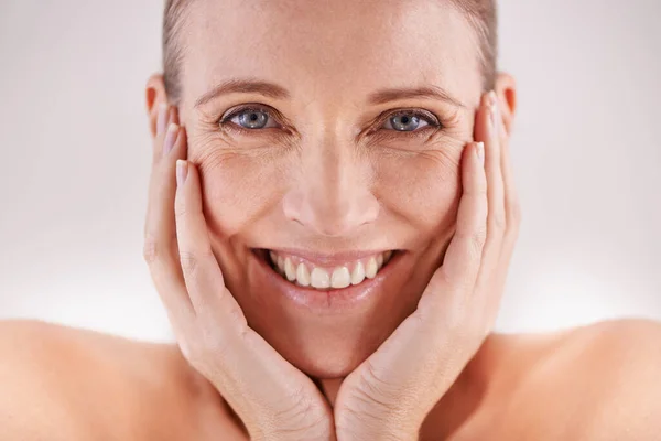 Shes still radiantly beautiful. Studio portrait of a happy mature woman posing with her head in her hands. — Stock Photo, Image