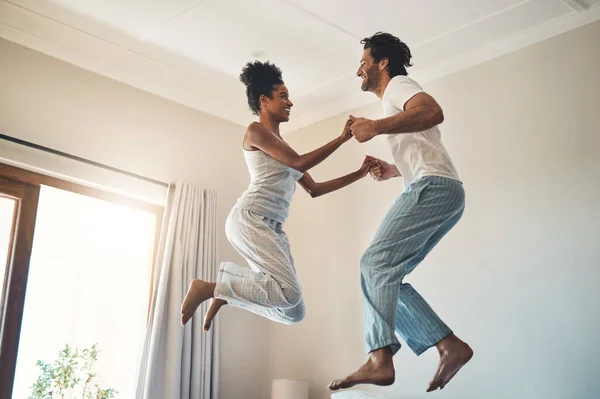 Taking each other to newer heights. Full length shot of an affectionate young couple jumping playfully on their bed at home. — Stock Photo, Image