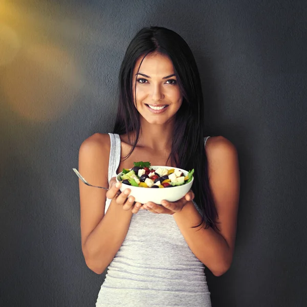 Det är en skål full av godhet. Porträtt av en frisk ung kvinna som äter en sallad mot en grå bakgrund. — Stockfoto