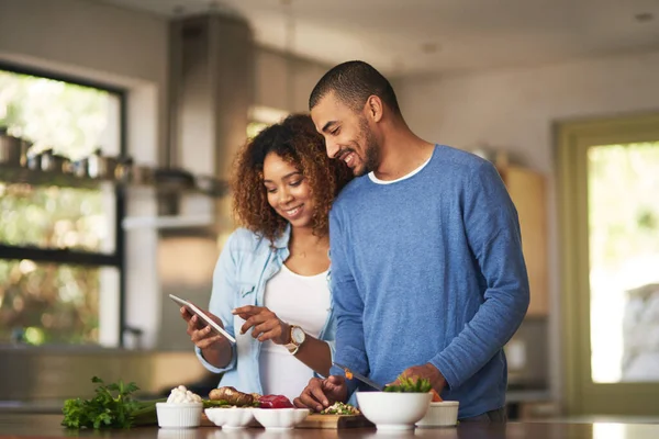 차근차근 온라인 레시피를 사용하는 거죠. 집에서 함께 건강에 좋은 식사를 준비하면서 디지탈 태블릿을 사용하는 행복 한 젊은 부부의 사진. — 스톡 사진