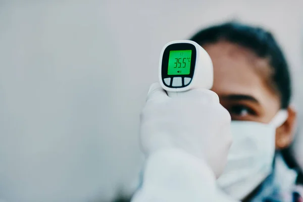 Cutting edge tech to help curb the spread. Shot of a young woman getting her temperature taken with an infrared thermometer by a healthcare worker during an outbreak. — Stock Photo, Image