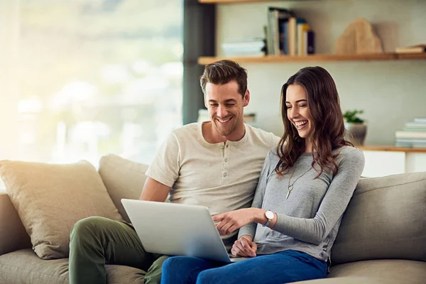 Condividere un mondo online. Girato di una giovane coppia felice utilizzando un computer portatile insieme sul divano di casa. — Foto Stock