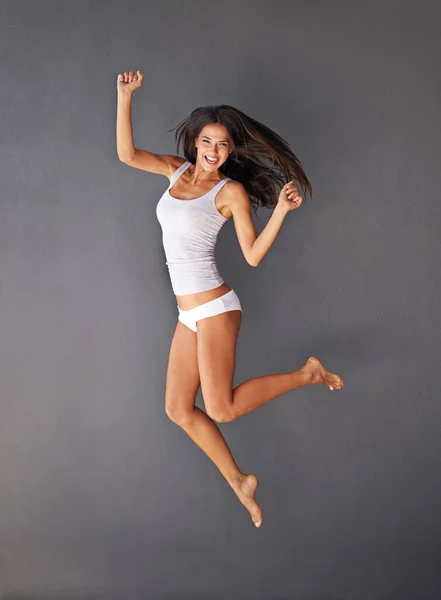 Полная жизни. Полнометражный снимок здоровой молодой женщины, прыгающей на сером фоне. — стоковое фото