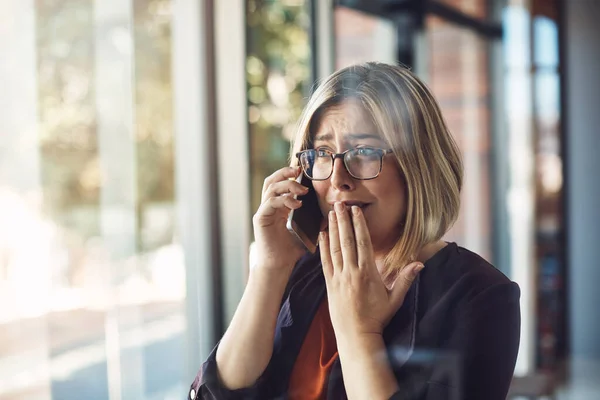 I det ögonblicket förändrades livet för alltid. Skjuten av en ung kvinna som ser upprörd ut när hon pratar i en mobiltelefon på ett modernt kontor. — Stockfoto