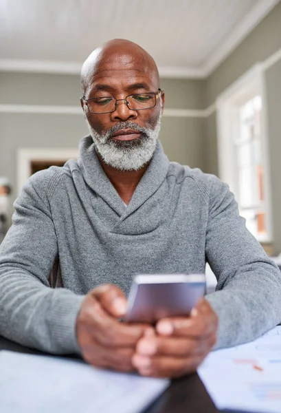 Теперь ты можешь брать деньги откуда угодно. Обрезанный снимок пожилого человека, использующего свой мобильный телефон, когда он работает над своими финансами дома. — стоковое фото