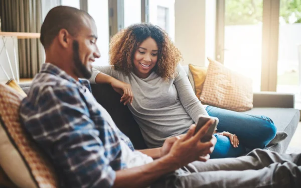 Zdravé manželství udržuje komunikační linky otevřené. Snímek mladého páru odpočívající na pohovce doma a pomocí mobilního telefonu spolu. — Stock fotografie