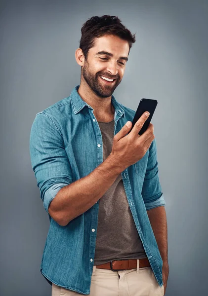 O texto que pôs um sorriso no seu mostrador. Estúdio tiro de um jovem bonito usando um telefone celular contra um fundo cinza. — Fotografia de Stock