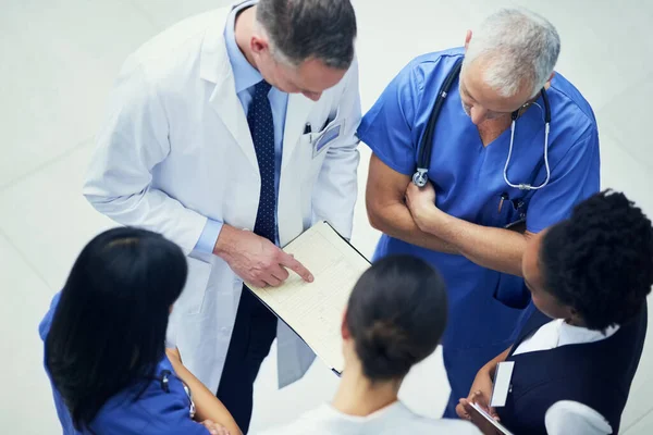 Discuter des diagnostics. Prise de vue d'un groupe de médecins parlant ensemble sur un dossier médical alors qu'ils se tenaient dans un hôpital. — Photo