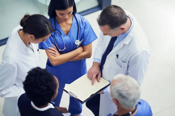 이 환자를 위해 투 여량을 늘려 주 세요. 한 무리의 의사들 이 병원에 서서 의학 차트를 놓고 함께 이야기하는 모습을 찍은 사진. — 스톡 사진