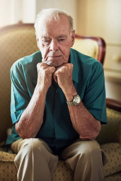 Waarin het leuk is om oud en alleen te zijn. Gehakt schot van een senior man die er verdrietig uitziet terwijl hij met zijn handen op zijn kin in een woonkamer zit. — Stockfoto