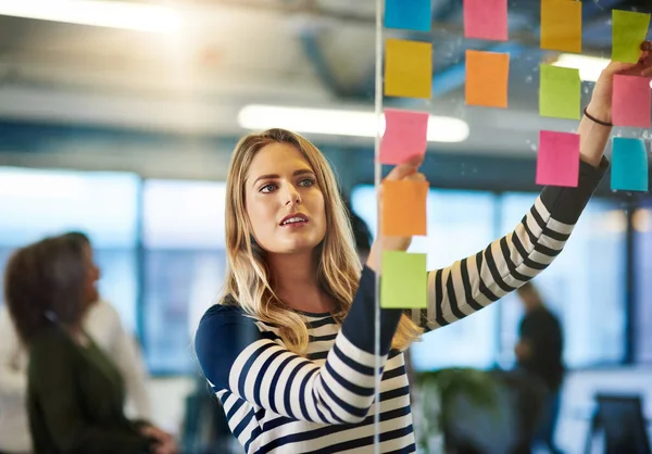 Uppnå framgång med en väl utarbetad plan. Skjuten av en ung kvinna som har en brainstorming session med klibbiga anteckningar på jobbet. — Stockfoto