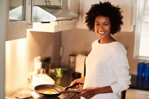 How do you like your eggs. Shot of a happy young woman cooking a fried egg at home. — Stock Photo, Image