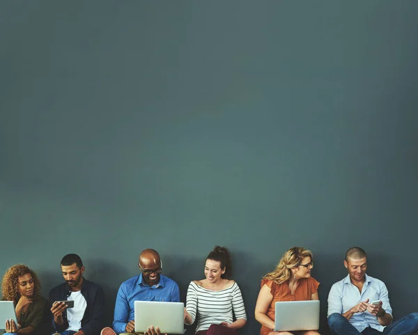 Verbinden terwijl we verbonden zijn. Studio shot van een diverse groep mensen social networking tegen een grijze achtergrond. — Stockfoto