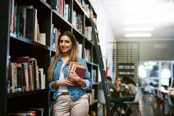 C'è molto da imparare in una biblioteca. Ritratto di una giovane donna felice che porta libri in una biblioteca al college. — Foto Stock