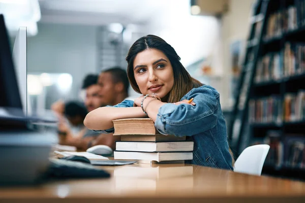 Ti rendero 'cosi' orgoglioso. Girato di una giovane donna a riposo su un mucchio di libri in una biblioteca del college e guardando premuroso. — Foto Stock