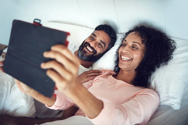 Se réveiller dans un monde sans fil. Tourné d'un couple d'âge mûr à l'aide d'une tablette numérique tout en se relaxant ensemble au lit. — Photo