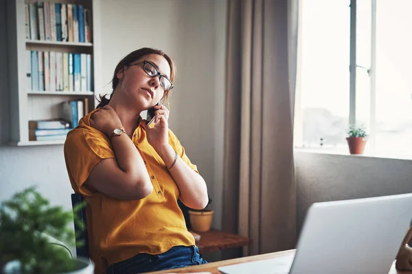 Llevo tanta tensión en el cuello. Recorte de una atractiva joven empresaria sentada sola en su oficina en casa y sintiéndose estresada mientras usa su teléfono celular. — Foto de Stock