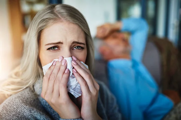 Non posso vincere questa lotta contro l'influenza. Ritratto di una donna che si soffia il naso con il marito sullo sfondo. — Foto Stock