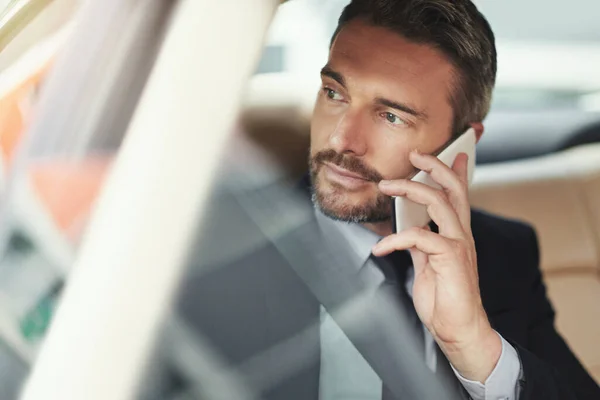 Ficar ligado no trajeto. Tiro de um homem de negócios usando seu telefone enquanto viaja em um carro. — Fotografia de Stock