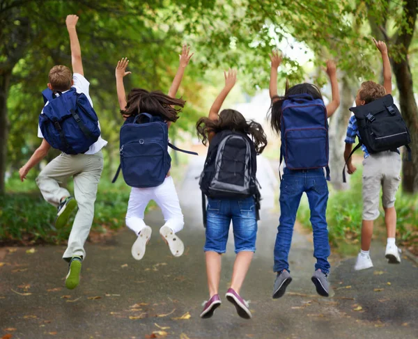Voorjaarsvakantie. Achteraanzicht van opgewonden schoolkinderen springen op een rij. — Stockfoto