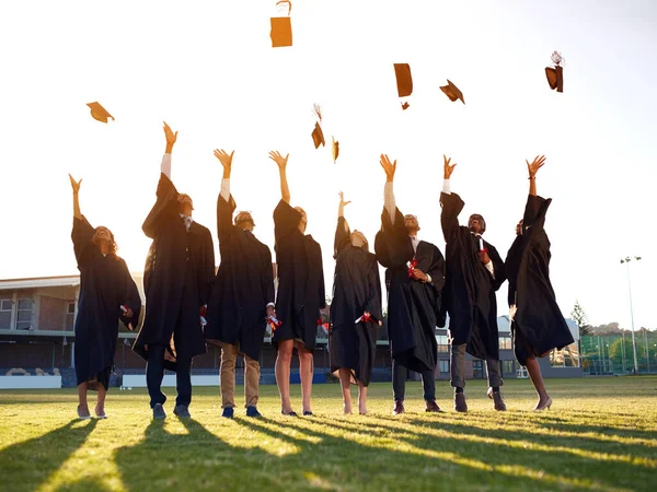 Osiągnęły one koniec lat akademickich. Strzał grupy studentów wyrzucających kapelusze w powietrze w dniu ukończenia szkoły.. — Zdjęcie stockowe