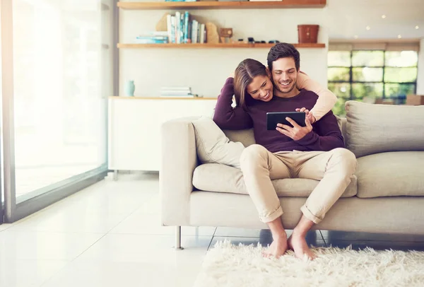 Estamos pegados como pegamento. Foto de una alegre pareja joven usando una tableta digital mientras se relaja en el sofá en casa. — Foto de Stock