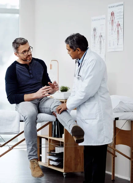 Jetons un coup d'oeil à ta jambe. Prise de vue d'un médecin masculin mature confiant effectuant un bilan de santé sur un patient à l'intérieur d'un hôpital pendant la journée. — Photo