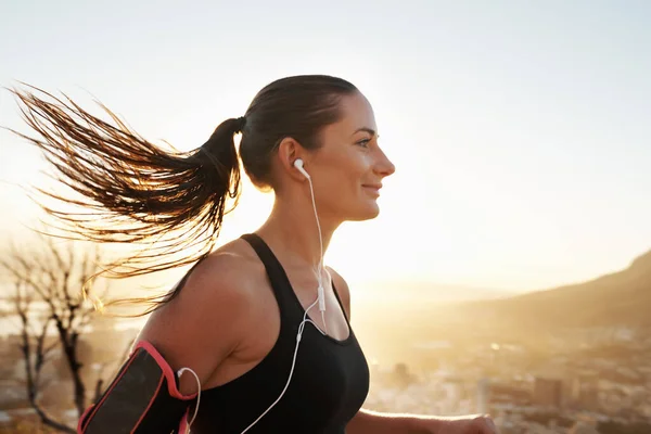 Those endorphins are kicking in. Shot of a young woman listening to music while out running. — Stock Photo, Image