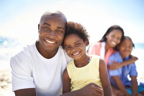 Samen het beste maken van de zon. Een dochter en vader genieten van een dag op het strand met moeder en broer op de achtergrond. — Stockfoto