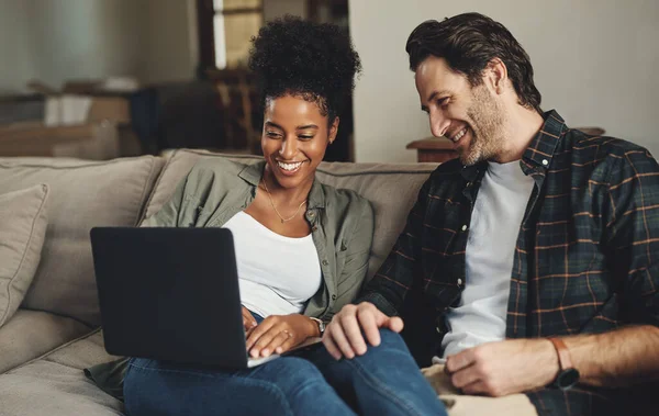 Estamos atualizando todos os nossos blogs hoje. Tiro de um jovem casal feliz usando um laptop enquanto relaxa em um sofá em sua sala de estar em casa. — Fotografia de Stock