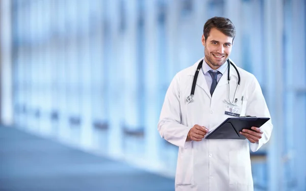 Redo att ställa en diagnos. Porträtt av en glad ung läkare som står i en sjukhushall med en patientjournal. — Stockfoto