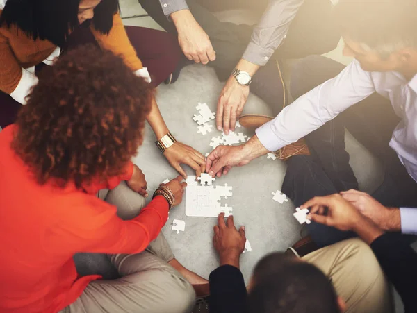 Piece by piece. High angle shot of a group of coworkers putting a puzzle together.