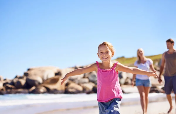 Fugir em liberdade. Uma menina correndo na frente de seus pais enquanto caminham na praia. — Fotografia de Stock